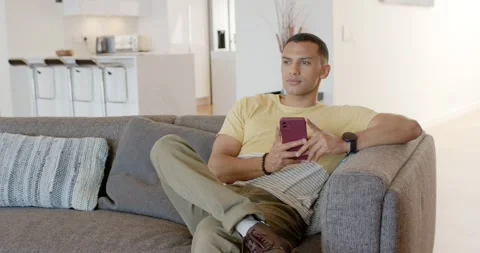 Man at home on couch scrolling pink smartphone pausing pondering glancing right, Stock Footage 336305853
