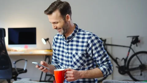 Man at home drinking coffee and using smartphone Stock Footage 126825702