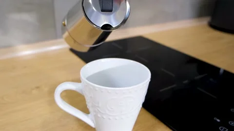 A man at home in the kitchen pours coffee from a coffee maker into a white cup Stock Footage 168572086