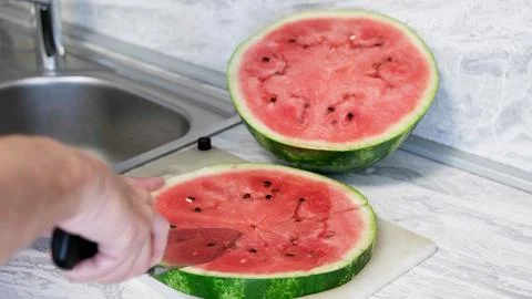 Man in home kitchen while cutting a ripe red watermelon in slices. Stock Photos