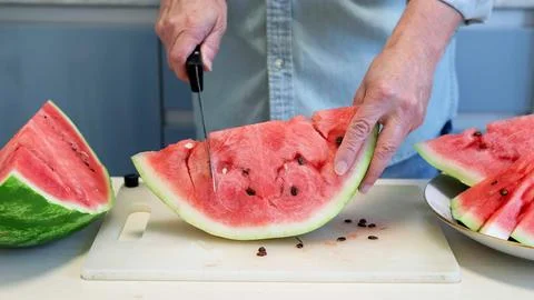 Man in home kitchen while cutting a ripe red watermelon in slices. Stock Photos