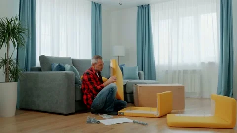 A man at home in the living room assembles a yellow lounge chair. Purchase and Stock Footage 166438470
