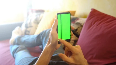 Man at Home Lying on a Couch using Smartphone with Green Mock-up Screen, hori Stock Footage 129654013