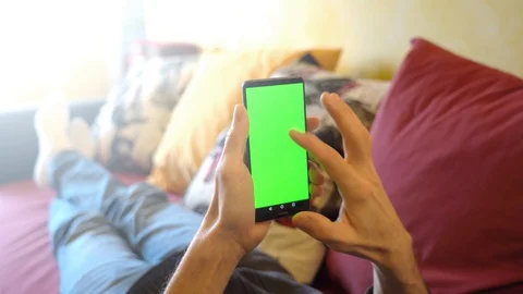 Man at Home Lying on a Couch using Smartphone with Green Mock-up Screen, vert Stock Footage 129654068
