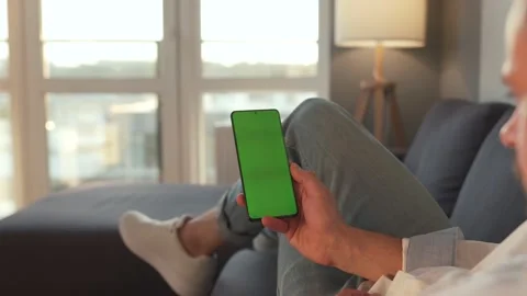 Man at home lying on a sofa and using smartphone with green mock-up screen in Stock Footage 141497767