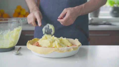 A man at home makes a pie with potatoes, cheese and sausages. Video stock 220190486