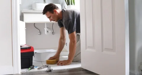 Man At Home Mopping Up Water From Leaking Pipe in Bathroom Stock Footage 120670660
