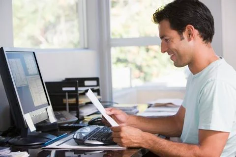 Man in home office using computer holding paperwork and smiling Stock Photos