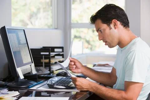 Man in home office using computer holding paperwork and looking shocked Stock Photos