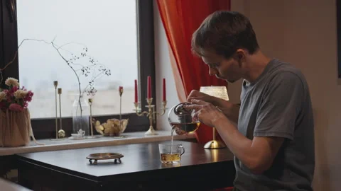 A man at home at a table by the window pours tea Stock-Footage 294254436