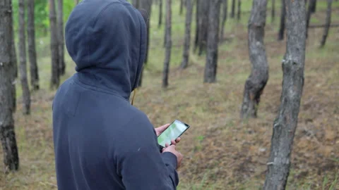 Man in a hood in the forest with a navigator in a smartphone Stock Footage 138401642
