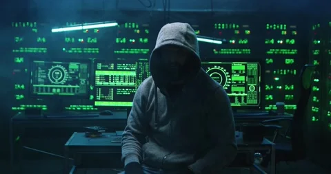 Man in hood hacked into database in office while sitting at computer turning in Stock Footage 145290944