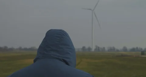 A Man In A Hood Stands Against The Backdrop Of A Spining Wind Generator Stock Footage 123690638