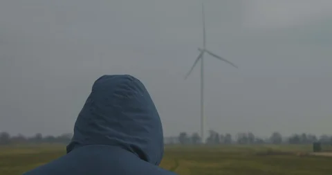 A Man In A Hood Stands Against The Backdrop Of A Rotating Wind Turbine.Windmills Stock Footage 123690651