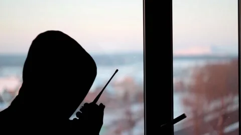 A man in a hood stands in front of the window and talks on a walkie-talkie Stock Footage 146775764