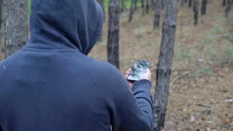 A man in a hood walks through the forest with a compass in a smartphone Stock Footage 138401430