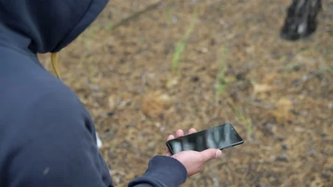 A man in a hood walks through the forest with a compass in a smartphone Stock Footage 138401550