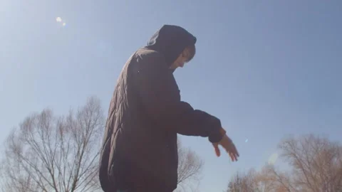 A man in a hooded jacket reflects by a railing, then pauses in a park Stock Footage 313432463