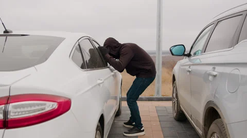 A man in a hooded jacket stands next to a white car Stock Footage 266797554