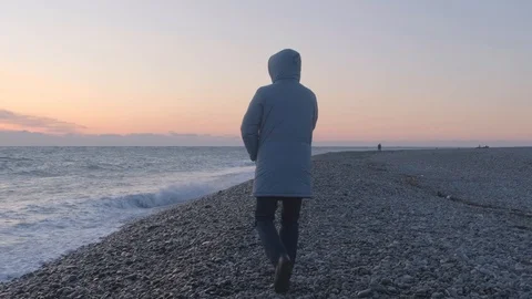 A man in a hooded jacket walks along the waterfront at sunset. A lonely man Stock Footage 120844779