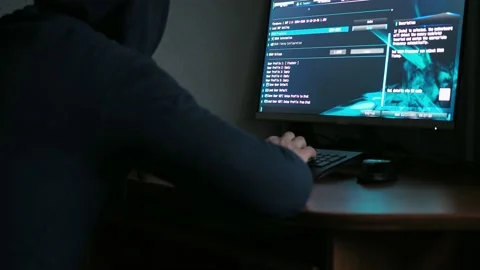 A man in a hooded sweatshirt is sitting at a computer in the dark. light from Stock Footage 167559440