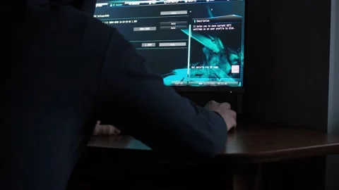 A man in a hooded sweatshirt is sitting at a computer in the dark. light from Stock Footage 167608799