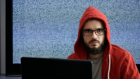 Man in hoodie using laptop and pointing at you with grainy screen behind Stock Footage 72091053