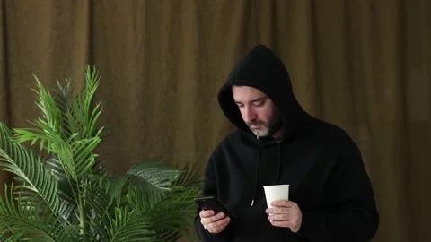 Man in hoodie using smartphoneand drinking coffee Stock Footage 233819594