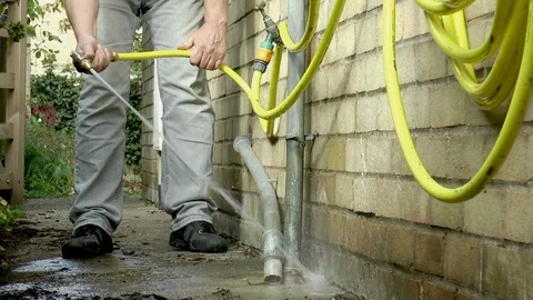 Man hosing down a drain at the side of a house. Video stock 96241795
