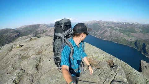 A man with a huge backpack walking at the edge of Preikestolen, Norway. He is Stock Footage 133396167