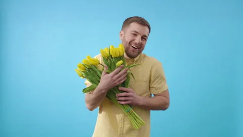 Man hugging bunch of yellow tulips on blue background Video stock 266452385