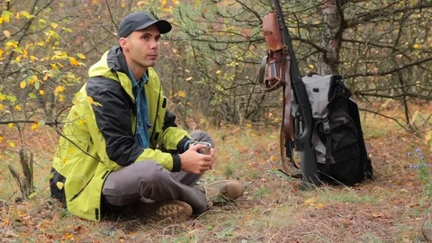 Man hunter resting in forest, drinking coffe. shotgun, ammunition, backpack Vídeos de archivo 97786731