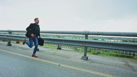 Man hurries down the highway with a briefcase in early morning light Видео 303798840