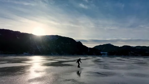 Man ice skating at sunset across frozen fjord in Norway Видео 331065632