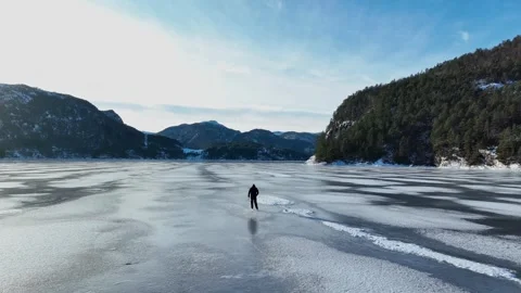 Man ice skating toward bright sun across frozen fjord in Norway Stock-Footage 331034289