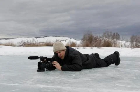 Man on ice with video camera looking into eyepiece Stock Photos
