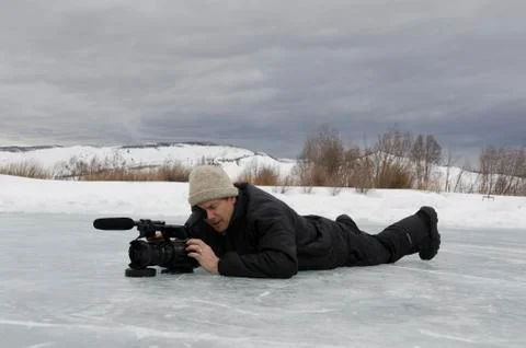 Man on ice with video camera looking into eyepiece Stock Photos