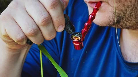 A man ignites marijuana in a pipe. A guy in a blue T-shirt smokes marijuana from Foto stock