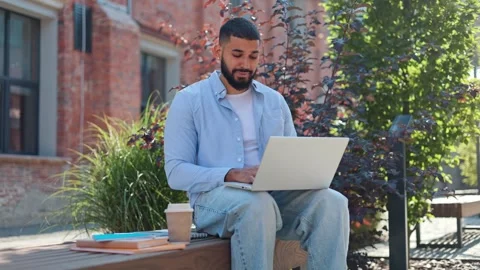 Man of indin ethnicity feeling overworked while sitting with computer on bench Video stock 250396065