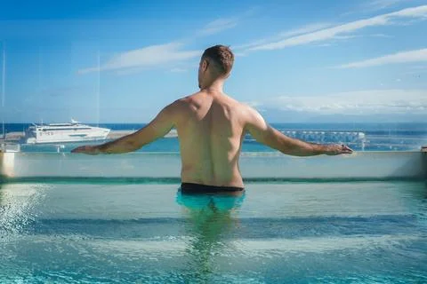 Man in Infinity Pool Overlooking Ocean with Yacht in Background Stock Photos