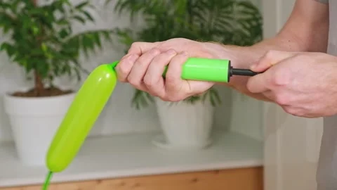Man inflates a balloon with a pump. Blowing green balloon by hand air pump Stock Footage 242444402