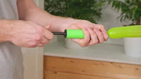 Man inflates a balloon with a pump. Blowing green balloon by hand air pump Stock Footage 243792309