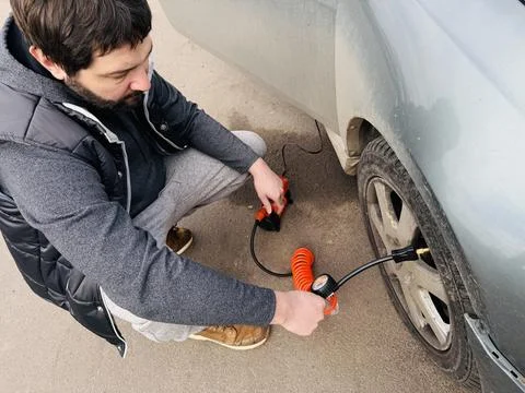 A man inflating a car tire using an electric air compressor . The scene shows Fotos de archivo