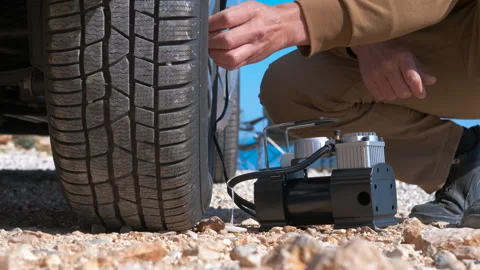 Man inflating a flat tire with a portable air compressor on a dusty road. Stock Footage 332791384