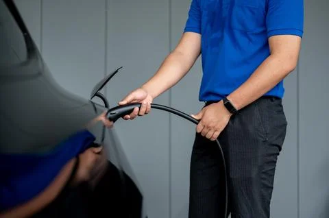 A man inserting a charging cable into his electric car at home, charging it.. Stock Photos