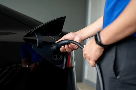 A man inserting a charging cable into his electric car at home, charging it.. Stock Photos