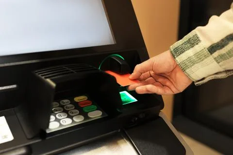 Man inserting orange credit card into ATM slot. Hand holding bank card at a.. Stock Photos