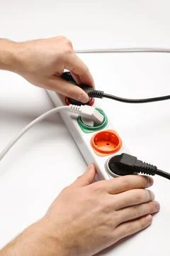 Man inserting power plug into extension cord on white background, closeup. El Stock Photos