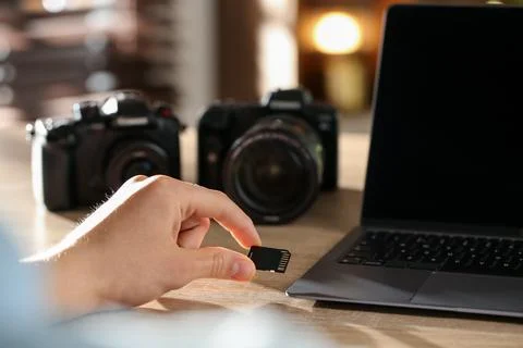 Man inserting SD memory card into laptop at wooden table indoors, closeup Stock Photos