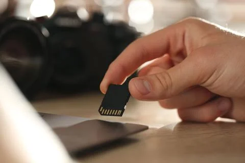 Man inserting SD memory card into laptop at wooden table indoors, closeup Stock Photos